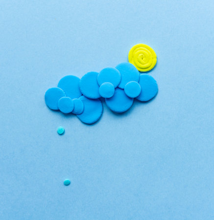 Plasticine sun with cloud and rain. Modeling clay handmade weather on blue background.の写真素材