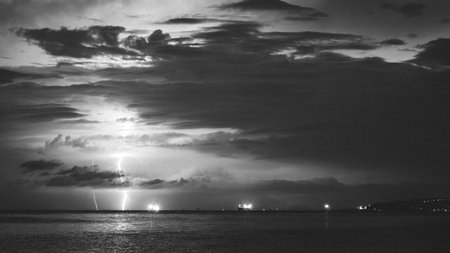 Epic photo of the sky over the sea with lightning in the clouds. Spectacular nature show. Long exposure photography, night landscape in black and whiteの写真素材