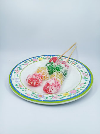 A food made from cassava starch. It tastes sweet and savory, red, yellow, green in color, which is skewered with bamboo sticks and sprinkled with grated coconut. Served on a small plate, with a flower patternの写真素材