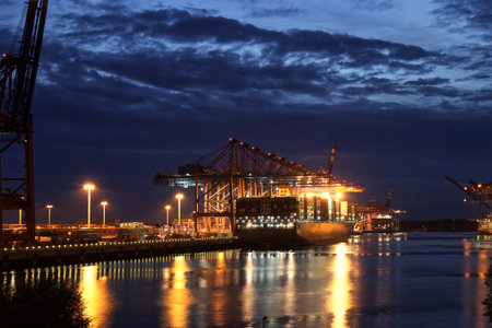 Illuminated Container Ship / Freighter at Dusk / Night in the port of Hamburg with big Gantry Cranes...