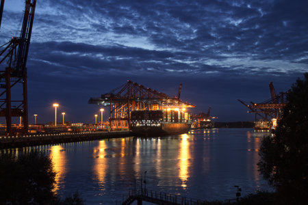 HAMBURG, AUGUST 2013: Illuminated Container Ship / Freighter at Dusk / Night (Magic Hour) in the port of Hamburg with big Gantry Cranes (Container Cranes). Beautiful Reflections in the water.のeditorial素材
