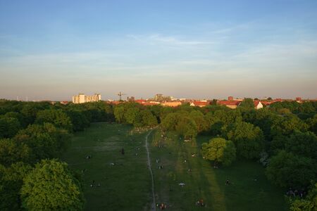 Aerial View of Berlin Park Hasenheide in Kreuzberg on an Spring afternoon with people relaxing and having fun on a large meadow in the sun. Behind the trees you can see roof tops of Berlin.の写真素材