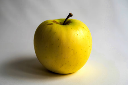a vibrant yellow apple centered against a stark white backgroundの写真素材