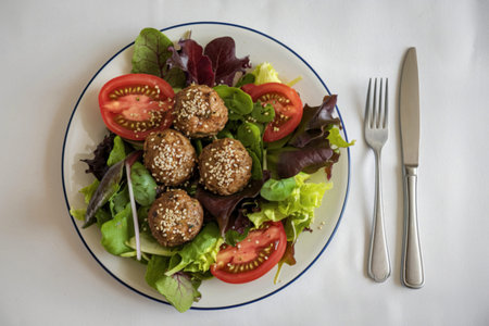 a plate of salad with tomatoes, green leaves, and meatballsの写真素材