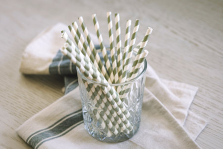 a clear glass cup with a pile of white and green striped paper strawsの写真素材