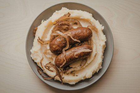 mashed potatoes with fried sausage and fried onions in a plateの写真素材