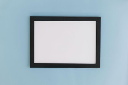 a black picture frame hangs on a light blue wall, the frame is rectangular and has a white interior