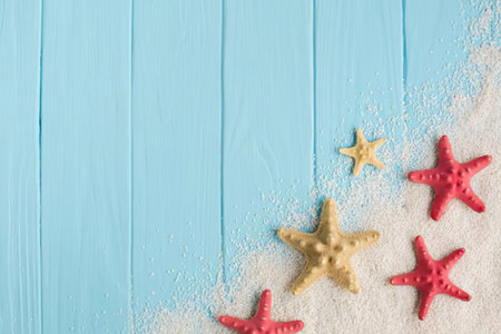 a group of starfish on a sandy beach with a light blue wooden background, the starfish are red and yellow