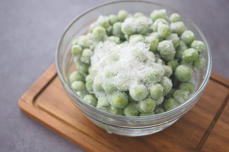Fresh green peas sprinkled with powdery seasoning in a clear glass bowl on wooden surface.
