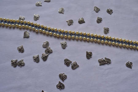 Silver beads in the shape of a heart and beads on a white background. Goods for creativity and needlework.の写真素材