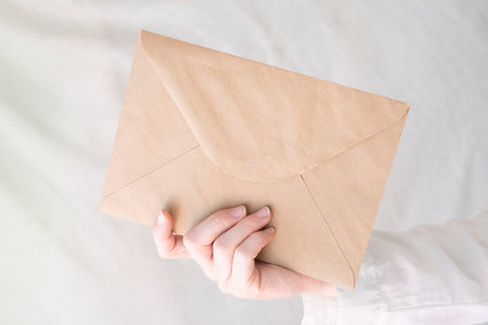 Female hand holding an ecological envelope with empty wall background