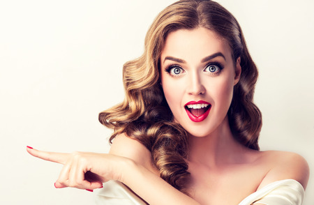 Surprised woman demonstrates invisible product .Beautiful girl with curly hair pointing to the side. Bright facial expression.