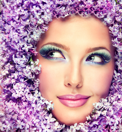 Gorgeous womans face surrounded by lilac flowers.Bright lavender-color make up. Tricky smile with glance to the side.の写真素材