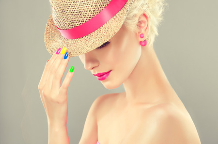 Stylish blonde girl in a straw hat with bright pink makeup and earrings-beads, multicolored nail polish on her nails.Spring and summer look.の写真素材