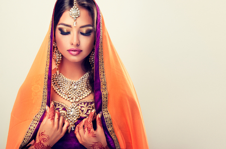 Portrait of beautiful indian girl dressed in a traditional national suit-sari,  mehndi henna tattoo is  painted on her hands and traditional kundan style jewelry set. Black haired indian young woman put on  in a posh outfit lehenga choli.の写真素材