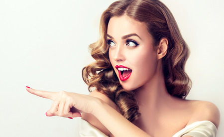 Surprised woman indicates to invisible product .Beautiful girl with curly hair pointing to the side. Bright facial expression of excitement, admiration.の写真素材