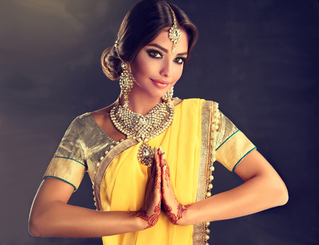 Portrait of beautiful indian girl dressed in a traditional national suit,  mehndi henna tattoo is  painted on her hands and traditional kundan style jewelry set  is showing a gesture of greeting - namaste.