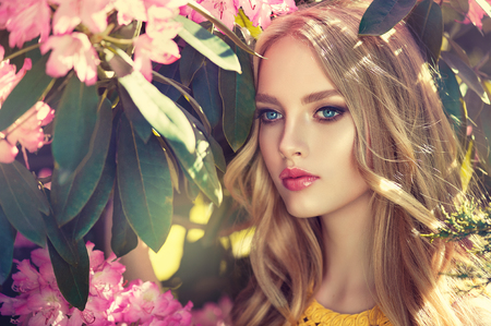 Magnificent young woman surrounded by blossoming flower trees. Gentle makeup, rose lipstick and freely lying long hair curls.の写真素材
