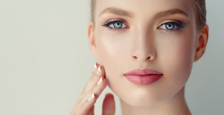 Gorgeous, young, woman with clean fresh skin, gentle makeup and rose lipstick on the lips is touching the face. Close-up portrait in a soft focus. Facial treatment, cosmetology, beauty technologies and spa.の写真素材