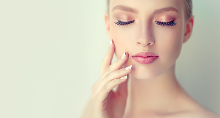Gorgeous, young, woman with clean fresh skin, gentle makeup and rose lipstick on the lips is touching the face. Close-up portrait in a soft focus. Facial treatment, cosmetology, beauty technologies and spa.の写真素材