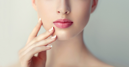 Gorgeous, young woman is touching the face by graceful fingers of hand, light-pink manicure on her nails. Close-up detail of human face.Facial treatment, cosmetology and beauty technologies.の写真素材