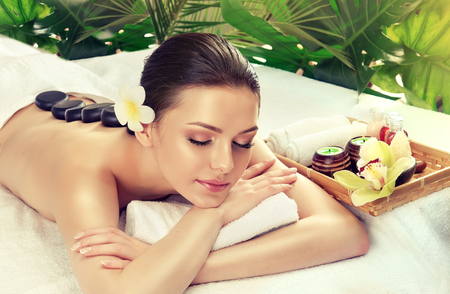 Young attractive woman is undergoing of  stone therapy. Spa and body massage, recuperation and traditional healthcare methods.の写真素材