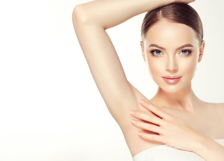 Young, brown haired woman with clean fresh skin and hair gathered in neat hairstyle is touching tenderly clean shaved armpit.の写真素材