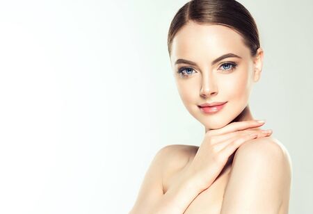 Gorgeous, young, brown haired woman with clean fresh skin and hair gathered in neat  hairstyle is touching the face. Facial treatment, cosmetology, beauty technologies and spa.の写真素材