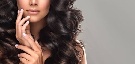 Brown haired woman  with voluminous hair is touching tenderly own face. Beautiful model with long, dense, curly hairstyle and vivid makeup.の写真素材