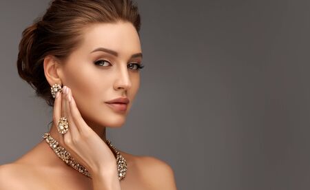 Portrait of alluring woman dressed in a posh jewelry set of necklace, ring and earrings. Pretty model is gazing at the viewer by magnetic look, perfect evening makeup and hair gathered in elegant bun.の写真素材