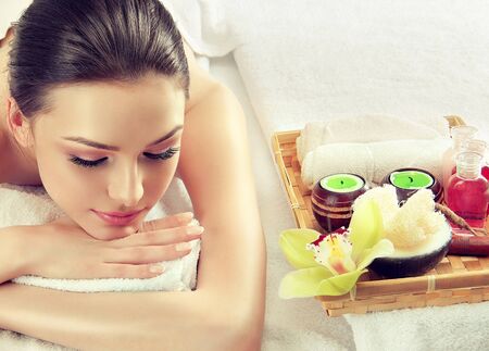Young,relaxed woman is laying on massage table surrounded by comfort atmosphere of spa salon. Spa and body massage, recuperation and traditional healthcare methods.の写真素材