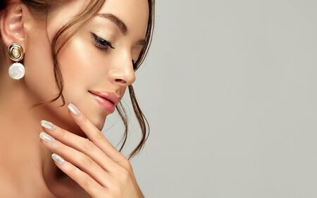 Close-up portrait of woman dressed in splendid evening makeup. Lips painted in pale rose color and long black eyelashes. Trendy style earrings with natural seashells in her ears.の写真素材