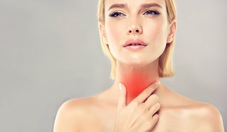 Young, attractive woman is touching the neck with expression of sharp pain on the face. Symbolic image of sore throat, any type of inflammation, endocrinology problems, thyroid gland diseases.の写真素材