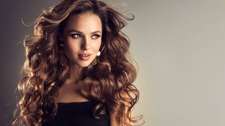 Flying hair, pretty smile and emotional look. Beautiful model with long, dense, curly hairstyle and vivid makeup. Bold and dazzling look of beautiful lady.の写真素材
