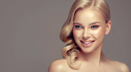 Portrait of beautifully looking young blonde haired woman, dressed in a delicate evening makeup.Perfect model with wide, toothy smile on the face. Beauty, elegance, hairstyling, cosmetic and dentistry.の写真素材