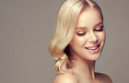 Portrait of beautifully looking young blonde haired woman, dressed in a delicate evening makeup.Perfect model with wide, toothy smile on the face.  Beauty, elegance, hairstyling, cosmetic and dentistry.の写真素材