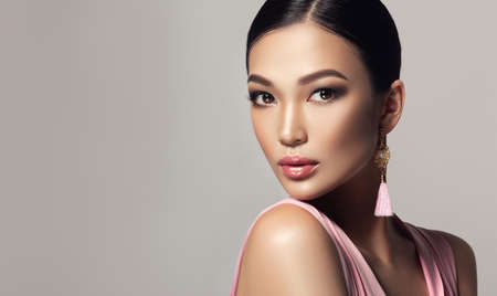 Black haired young woman with asian appearance is demonstrating dense, well cared, straight hair and vivid evening makeup on the face.Oriental beauty. Hairdressing art, hair care and beauty products.の写真素材