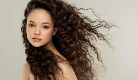 Beautiful face of young and gorgeous woman in delicate makeup, surrounded by flying hair. Sincere look in the eyes of viwer. Long, dense, curly hair. Innocence of youth.の写真素材