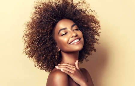 Portrait of perfectly looking brown haired young woman. Natural, dense afro hair on the head of young beautiful model, white toothy smile on her face. Girl with vibrant, melanin-rich skin tone.の写真素材