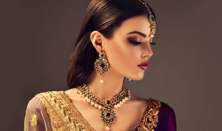 Gorgeous black haired woman in a splendid makeup with smokey eyeshadows and red lipstick, dressed in a traditional indian blouse and national jewellery set.Indian beauty.の写真素材