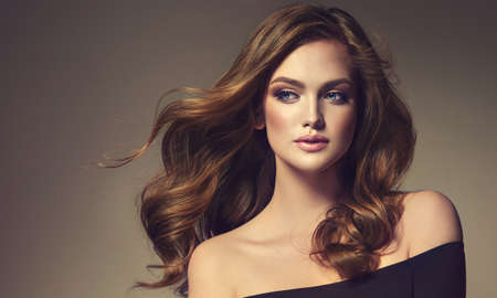 Young, brown haired beautiful model with long, wavy, well groomed hair. Excellent hair waves. Hairdressing art and hair care.の写真素材