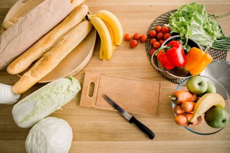 Fresh fruits and vegetables for salad, wooden board and knife on a kitchen table. Healthy foods, cooking and vegetarian concept.の写真素材