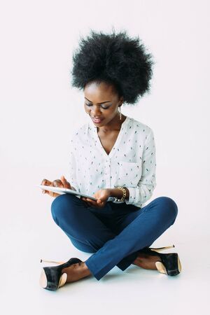 Young african american business woman using the tablet while sitting on the floor, isolated on whiteの写真素材