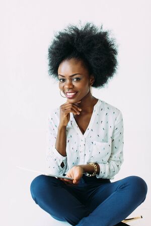 Young african american business woman using the tablet while sitting on the floor, isolated on whiteの写真素材