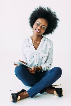 Young african american business woman using the tablet while sitting on the floor, isolated on whiteの写真素材