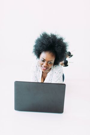 Young african american business woman using the laptop, while lying on the floor, isolated on white backgroundの写真素材