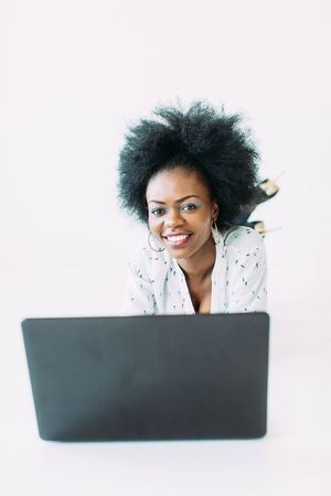 Young african american business woman using the laptop, while lying on the floor, isolated on white backgroundの写真素材