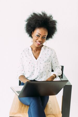 Young african american business woman typing on laptop while sitting on the chair, isolated on whiteの写真素材