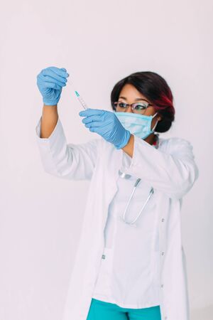 Young smiling African American doctor in medical mask holding a syringeの写真素材