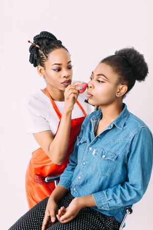 Young beautiful African American woman applying professional make-up by African make-up artist. Studio shootの写真素材